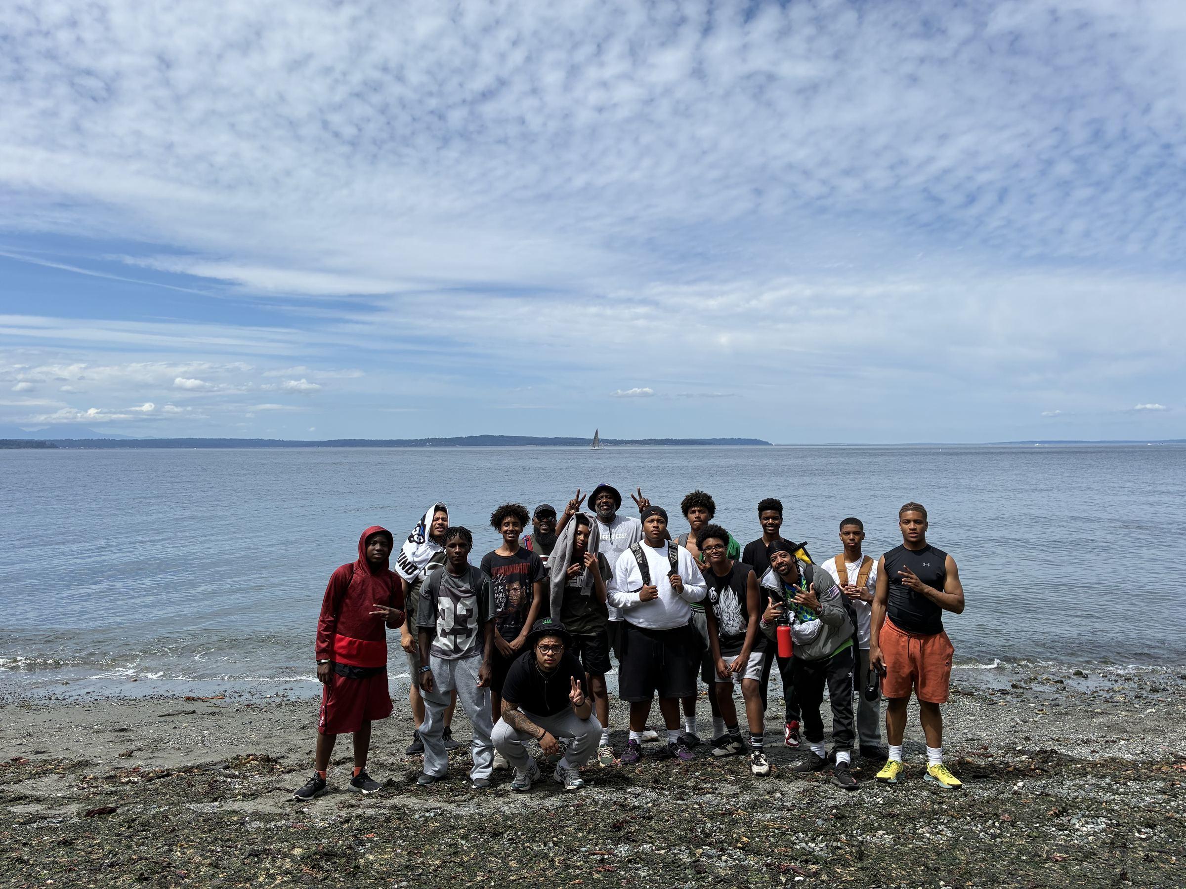 A group of Standing Tall Collective youth and mentors standing together on a Washington State beach, smiling and celebrating.